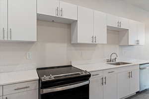 Kitchen with appliances with stainless steel finishes, white cabinetry, light stone counters, and sink