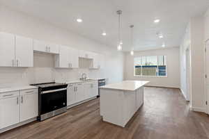 Kitchen featuring stainless steel appliances, white cabinets, a center island, decorative light fixtures, and dark hardwood / wood-style floors