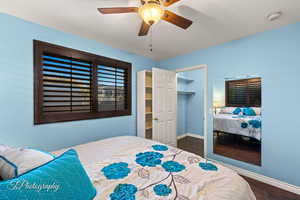 Bedroom with a walk in closet, a closet, ceiling fan, and dark wood-type flooring