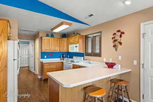 Kitchen with white appliances, a kitchen bar, lofted ceiling, and kitchen peninsula