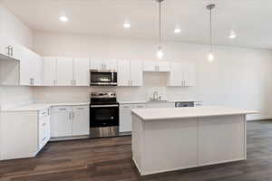 Kitchen featuring stainless steel appliances, white cabinetry, hanging light fixtures, and dark wood-type flooring