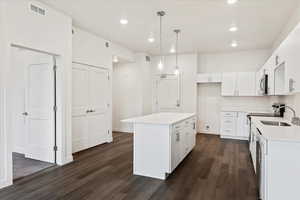 Kitchen with stainless steel appliances, hanging light fixtures, a center island, dark wood-type flooring, and white cabinetry