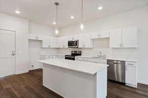 Kitchen featuring stainless steel appliances, sink, decorative light fixtures, white cabinets, and dark wood-type flooring