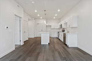 Kitchen with appliances with stainless steel finishes, decorative light fixtures, a center island, white cabinets, and dark wood-type flooring