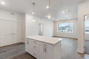 Kitchen featuring a textured ceiling, hanging light fixtures, a kitchen island, dark hardwood / wood-style flooring, and white cabinets