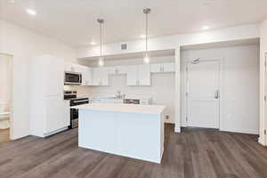 Kitchen with appliances with stainless steel finishes, white cabinets, a center island, pendant lighting, and dark wood-type flooring