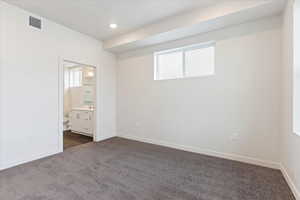 Unfurnished bedroom with ensuite bath and dark carpet