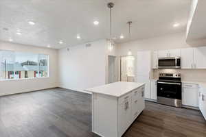 Kitchen with decorative light fixtures, a center island, appliances with stainless steel finishes, and white cabinetry