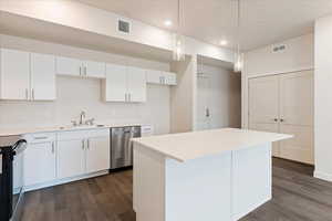 Kitchen with black range with electric cooktop, sink, white cabinetry, decorative light fixtures, and stainless steel dishwasher