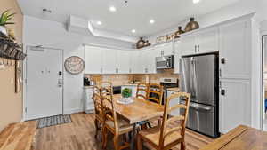 Kitchen featuring light hardwood / wood-style floors, white cabinets, backsplash, and appliances with stainless steel finishes