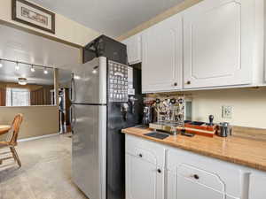 Kitchen featuring white cabinetry, light tile patterned flooring, ceiling fan, track lighting, and stainless steel fridge