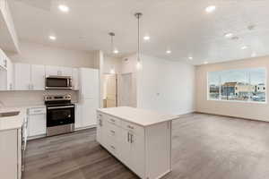 Kitchen with appliances with stainless steel finishes, a center island, white cabinets, decorative light fixtures, and sink