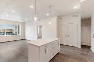 Kitchen featuring dark wood-type flooring, a textured ceiling, pendant lighting, a kitchen island, and white cabinets