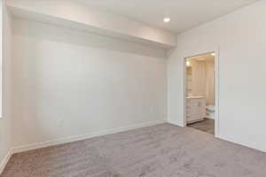 Unfurnished bedroom featuring ensuite bathroom and dark colored carpet