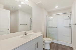 Bathroom featuring toilet, wood-type flooring, vanity, and a shower with shower door