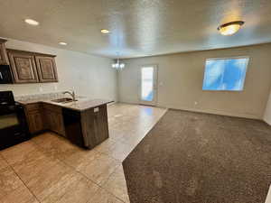 Kitchen with kitchen peninsula, light tile patterned floors, black appliances, an inviting chandelier, and sink