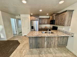 Kitchen with light stone counters, kitchen peninsula, black appliances, and sink