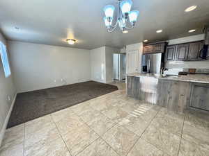 Kitchen with stainless steel fridge, light stone counters, dark brown cabinetry, sink, and an inviting chandelier