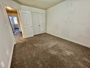 Unfurnished bedroom featuring dark carpet, a closet, and a textured ceiling