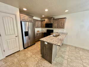 Kitchen featuring kitchen peninsula, light stone countertops, a textured ceiling, black appliances, and sink