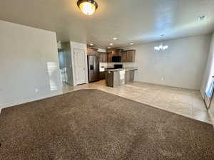 Kitchen with light tile patterned flooring, stainless steel fridge with ice dispenser, a kitchen island, a chandelier, and pendant lighting