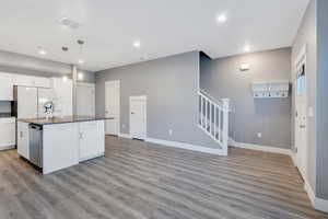 Kitchen featuring white fridge, stainless steel dishwasher, a kitchen island with sink, and white cabinetry