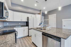 Kitchen featuring stainless steel appliances, sink, decorative light fixtures, white cabinetry, and a kitchen island with sink