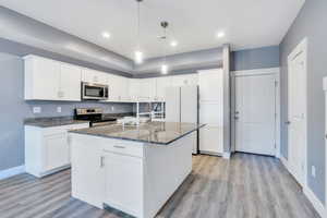 Kitchen with light hardwood / wood-style floors, stainless steel appliances, white cabinetry, and a kitchen island with sink