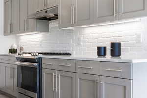 Kitchen with backsplash, stainless steel gas range, and gray cabinets