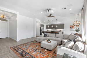 Living room featuring sink, light hardwood / wood-style flooring, lofted ceiling, and ceiling fan with notable chandelier