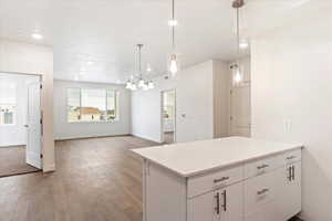 Kitchen featuring white cabinets, light stone counters, hardwood / wood-style flooring, hanging light fixtures, and a notable chandelier