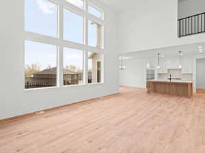 Unfurnished living room with light wood-style flooring, a chandelier, baseboards, visible vents, and a towering ceiling
