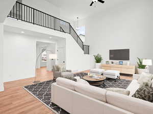 Living area featuring stairs, ceiling fan, a high ceiling, and wood finished floors