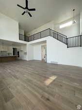 Unfurnished living room featuring ceiling fan, light wood-type flooring, and a towering ceiling