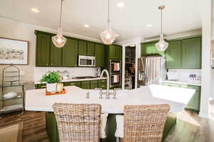 Kitchen featuring stainless steel appliances, decorative light fixtures, a kitchen island with sink, and green cabinets