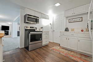 Kitchen with dark hardwood / wood-style floors, white cabinetry, and stainless steel appliances