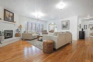 Living room featuring a chandelier, wood-type flooring, ornamental molding, and a brick fireplace