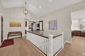 Hall with high vaulted ceiling, an inviting chandelier, and light wood-type flooring