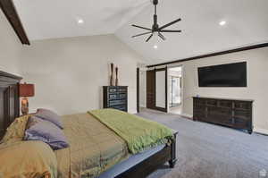 Carpeted bedroom featuring vaulted ceiling, ensuite bath, ceiling fan, and a barn door