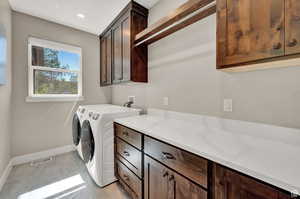 Laundry area with independent washer and dryer, cabinets, and light tile patterned flooring