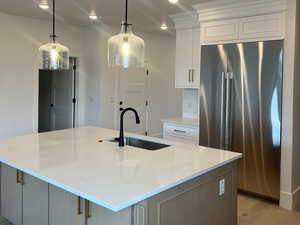 Kitchen with sink, white cabinets, a large island with sink, hanging light fixtures, and stainless steel fridge