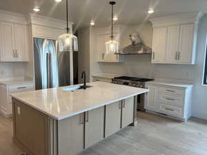 Kitchen featuring appliances with stainless steel finishes, white cabinetry, decorative light fixtures, and a kitchen island with sink