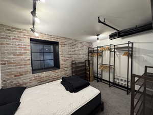 Bedroom featuring track lighting, carpet floors, and brick wall