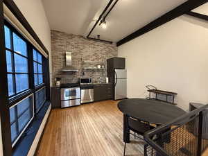 Kitchen featuring stainless steel appliances, wall chimney exhaust hood, light wood-type flooring, a baseboard heating unit, and brick wall