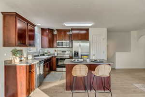 Kitchen with a breakfast bar area, light hardwood / wood-style floors, stainless steel appliances, a kitchen island, and sink