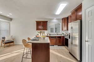 Kitchen featuring stainless steel appliances, sink, a center island, a kitchen breakfast bar, and light wood-type flooring