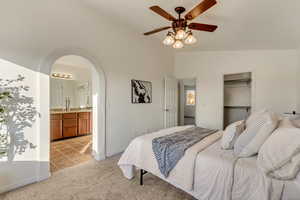 Carpeted bedroom featuring ceiling fan, sink, ensuite bath, and lofted ceiling