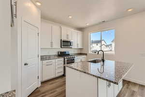 Kitchen with a center island with sink, light hardwood / wood-style floors, stainless steel appliances, sink, and white cabinetry