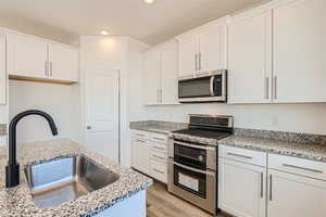 Kitchen with appliances with stainless steel finishes, light hardwood / wood-style floors, light stone counters, sink, and white cabinetry