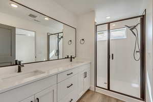 Bathroom with a sink, a shower stall, double vanity, and wood finished floors